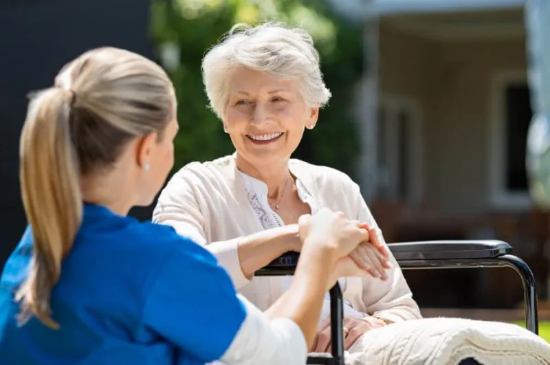 A caregiver engages warmly with an elderly woman in a wheelchair, highlighting compassionate support and connection.