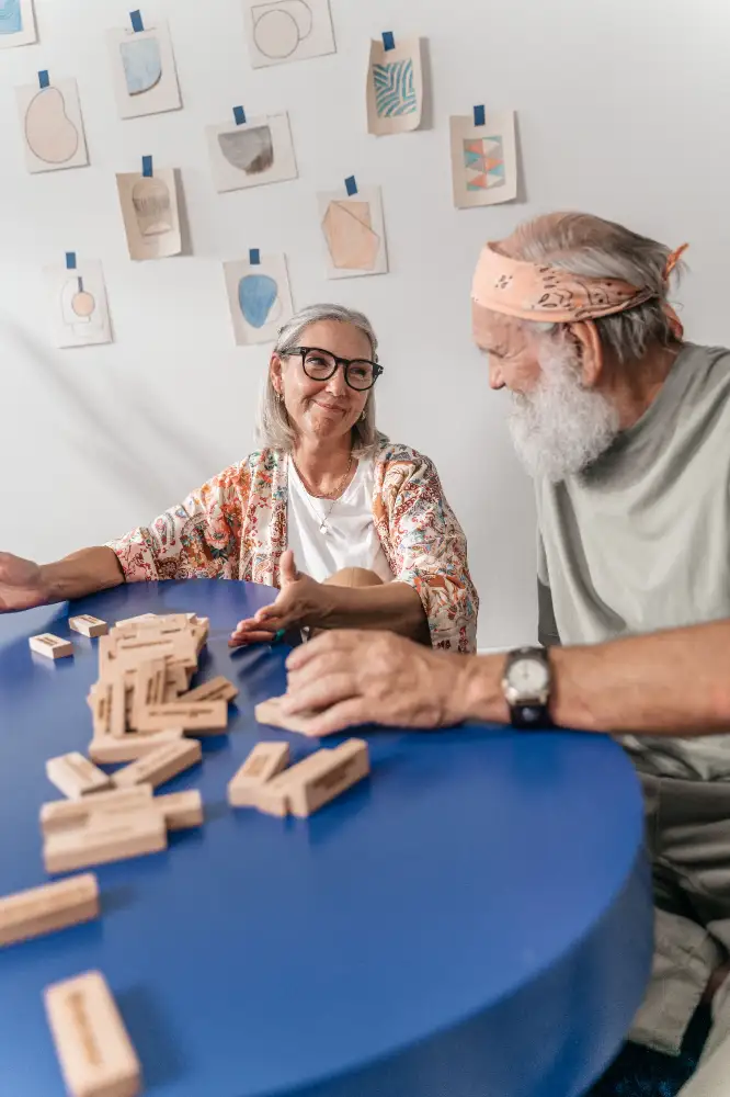 Seniors engage in a lively conversation while playing a game with wooden blocks at a blue table.