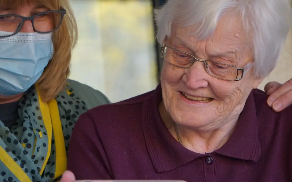 Two women, one elderly and one younger, share a joyful moment while looking at a smartphone together.
